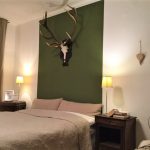 Grünes Schlafzimmer Blick 1 nachher mit grün abgesetzter Wand und Geweih über Bett, 2 Nachttische mit Nachttischlampen