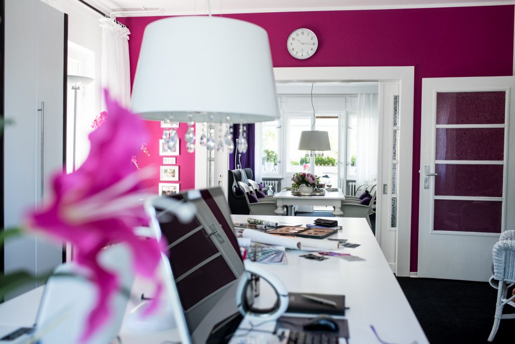 Ein Arbeitszimmer in Pink mit weißem Arbeitstisch und Lampe vor pinkfarbener Wand mit offener Schiebetür