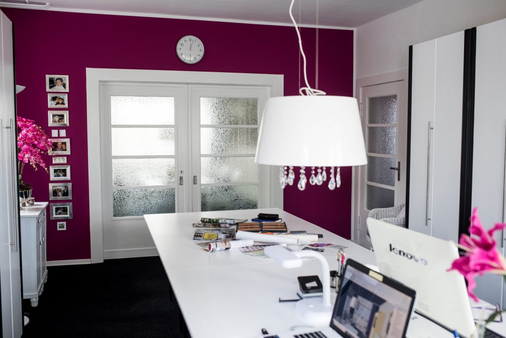 Ein Arbeitszimmer in Pink mit weißem Arbeitstisch und Lampe vor pinkfarbener Wand mit geschlossener Schiebetür