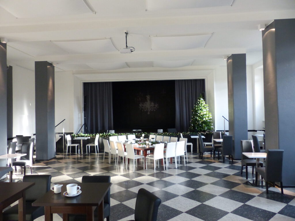 Aula Buehne teilbestuhlt nachher mit abgestimmten hellen und dunklen Tischen und Stuehlen