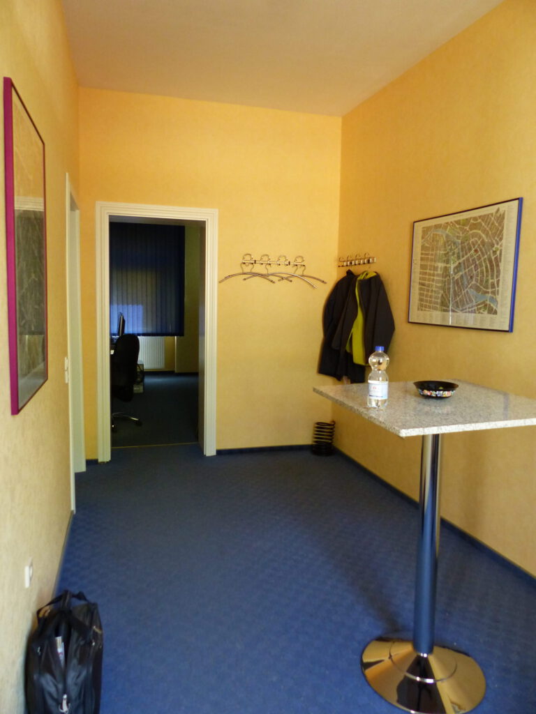 Schulungsraum vor Umgestaltung mit gelber Wand vor Stehtisch im Eingangsbereich
