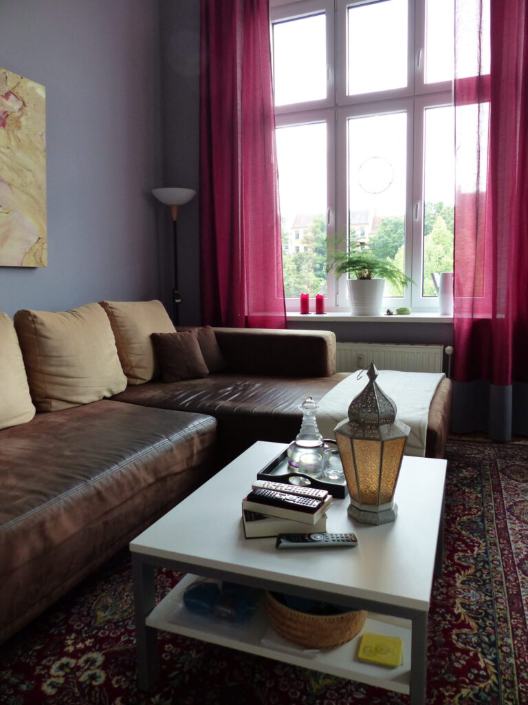 Wohnzimmer Blick 2 nachher mit Ecksofa, Couchtisch, grauer Wand und pinkfarbenen Vorhaengen