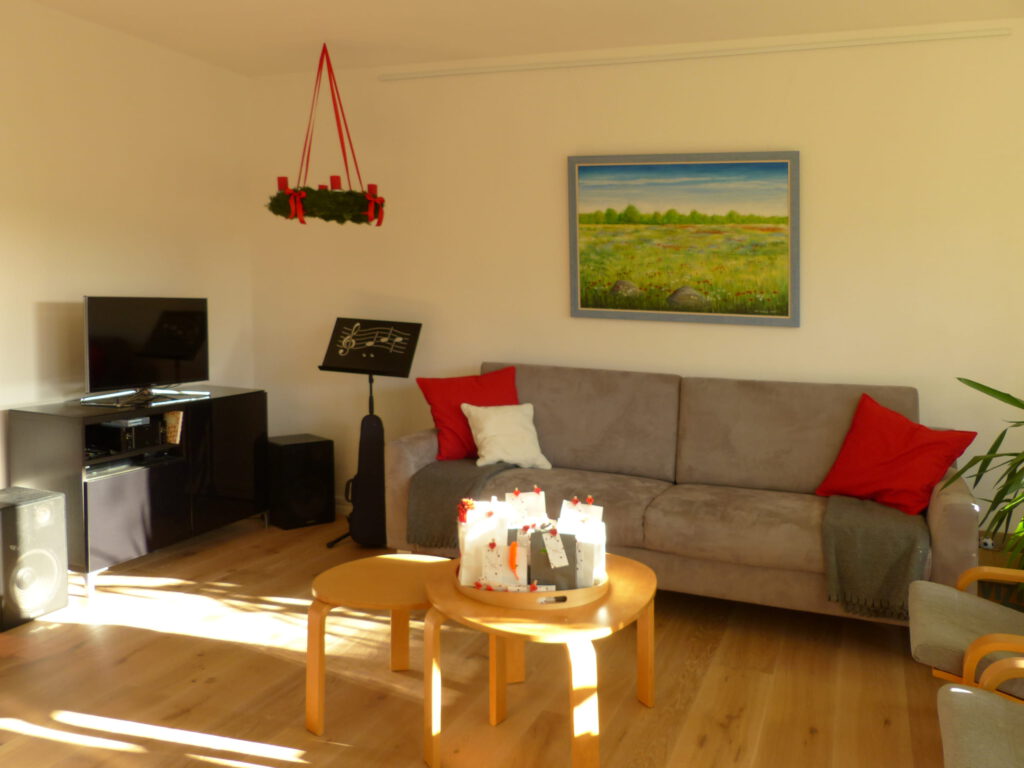 altes Klavier nach Umgestaltung mit schwarzem Fernseh-Sideboard und Notenständer, grauem Sofa und Wandbild