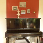 altes Klavier nach Umgestaltung mit Klavierhocker und weissen Bilderrahmen vor rotem Farbspiegel an der Wand