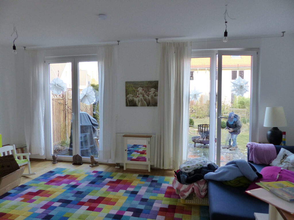 angezogenes Wohnzimmer vor Umgestaltung mit Polsterhocken vor Terrassentür