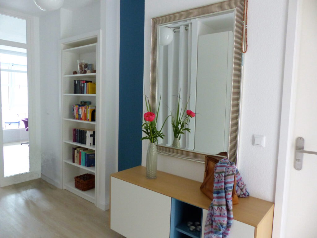 Flur Blick 1 nachher mit Wohnzimmertuer, Buecherregal in Tuer, blauem Wandteil, Sideboard und Spiegel