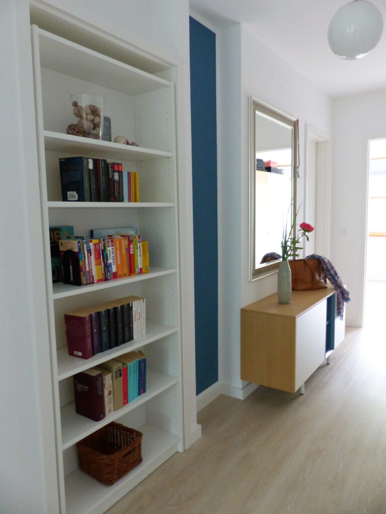 Flur Blick 3 nachher mit Buecherregal in Tuer, blauem Wandteil, Sideboard, Spiegel und Schlafzimmertuer