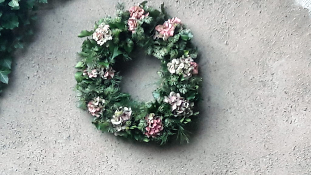 Kranz aus Hortensien, Tanne und Efeu vor grauer Gartenmauer