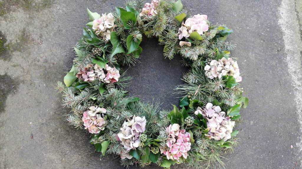 Kranz aus Hortensien, Tanne und Efeu mit vielen getrockneten Blüten vor grauer Gartenmauer