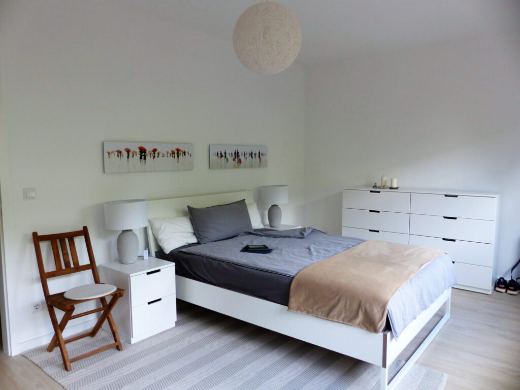 Schlafzimmer Blick 15 nachher mit Stuhl, Bett, Nachttischen, Lampen, Wandbildern und Schubladenelement