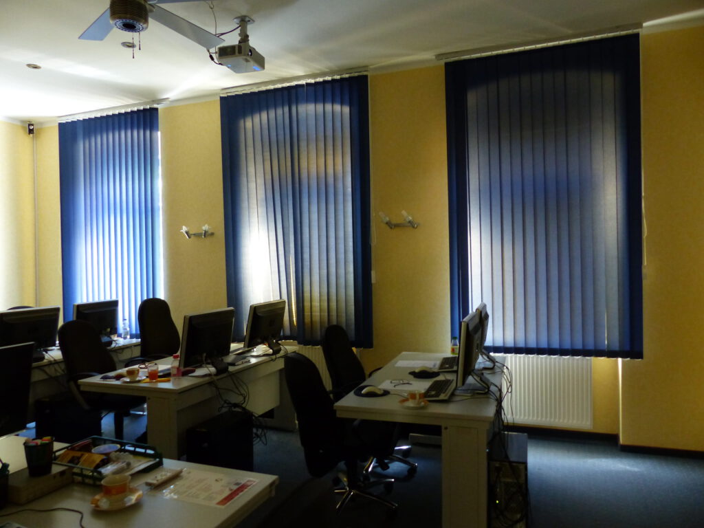 Schulungsraum vor Umgestaltung mit gelber Wand und blauen Vorhängen