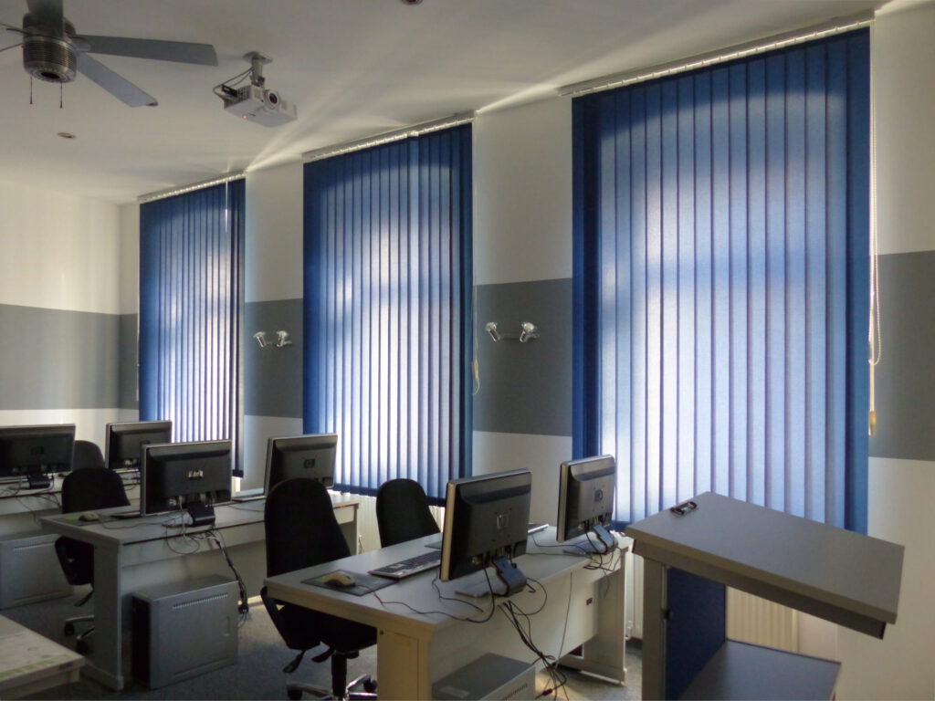 Schulungsraum nach Umgestaltung mit weißer Wand und grauem Farbstreifen und blauen Vorhängen