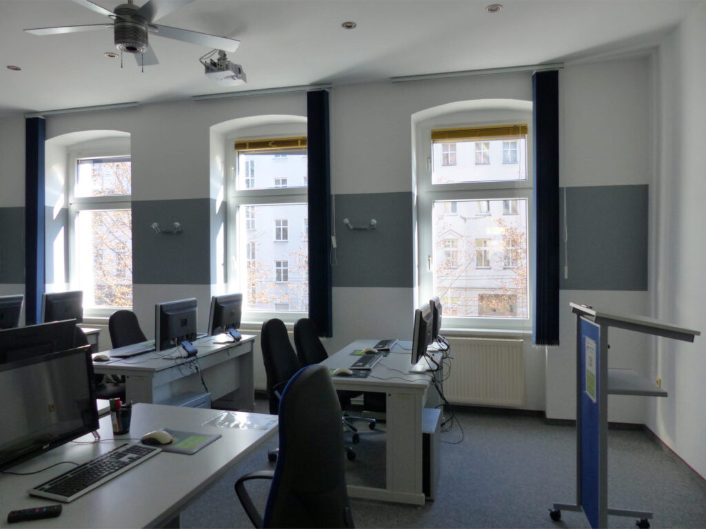 Schulungsraum nach Umgestaltung mit weißer Wand und Wandleuchten vor grauem Farbstreifen