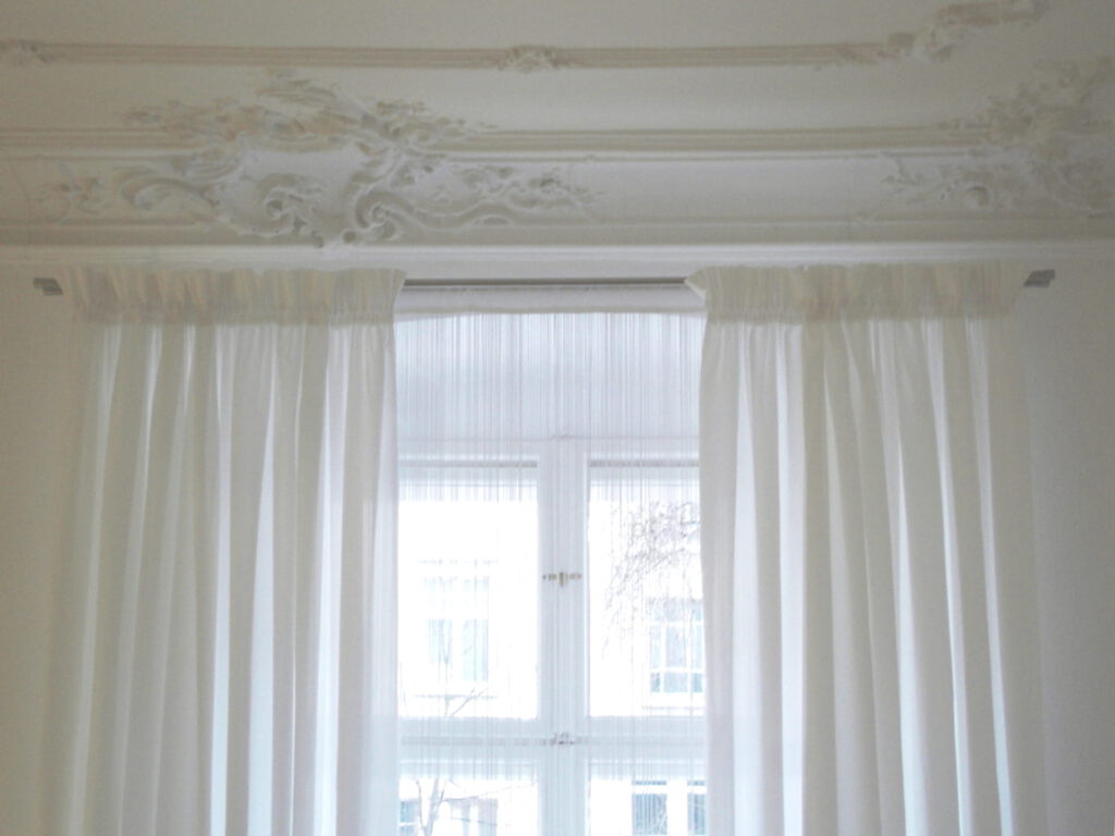 weisse Vorhaenge unter Stuckornamenten