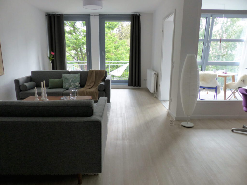 Wohnbereich Blick 5 nachher mit Zweisitzer, Couchtisch, Balkonfenster und Arbeitsraumabtrennung