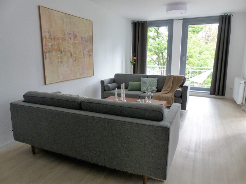 Wohnbereich Blick 5 nachher mit Zweisitzer, Couchtisch, Wandbild, Balkonfenster und Heizkoerper