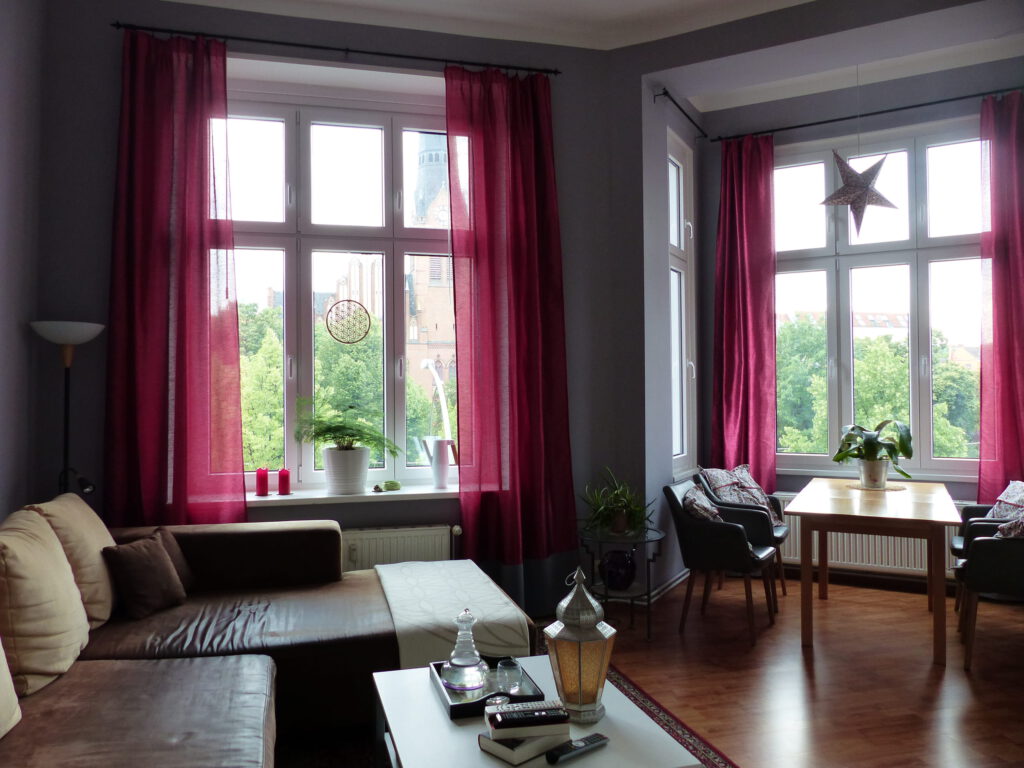 Wohnzimmer Blick 1 nachher mit Esstisch, Ecksofa und pinkfarbenen Vorhaengen